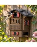 Koolmees vliegt met gespreide vleugels naar de invliegopening van de Multiholk Fjällstugan van Wildlife Garden, bevestigd aan een houten tuinschutting.