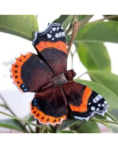 DecoButterfly Atalanta van Wildlife Garden als houten vlinderdecoratie tussen groene bladeren, met donkerbruine vleugels, oranjerode banden en witte vlekken.