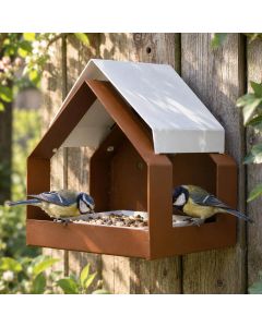 The Barn wandvoederhuis bruin van metaal met wit zadeldak, gemonteerd aan een houten schutting, waar twee koolmezen vogelvoer eten.