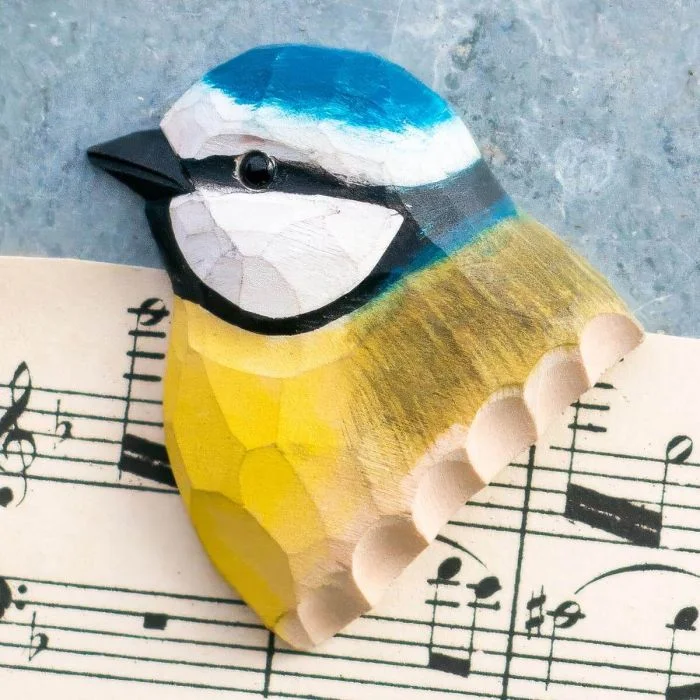 Houten koelkastmagneet Pimpelmees van Wildlife Garden met blauwe kruin, witte wangen, zwarte oogstreep en gele borst, gefotografeerd op bladmuziek.
