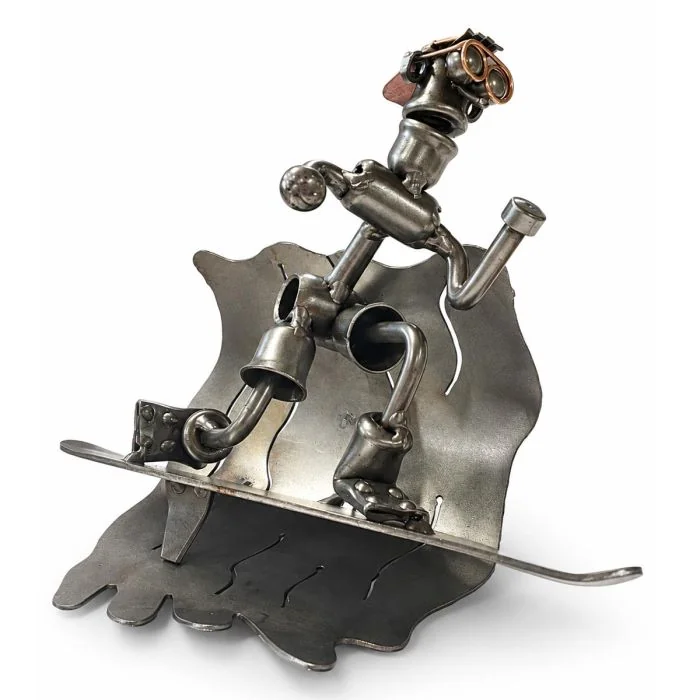 Metalen sculptuur van een surfer op een hoge golf met surfboard, pet en koperkleurige details. 15,3 cm hoog. Origineel cadeau voor een surfer.